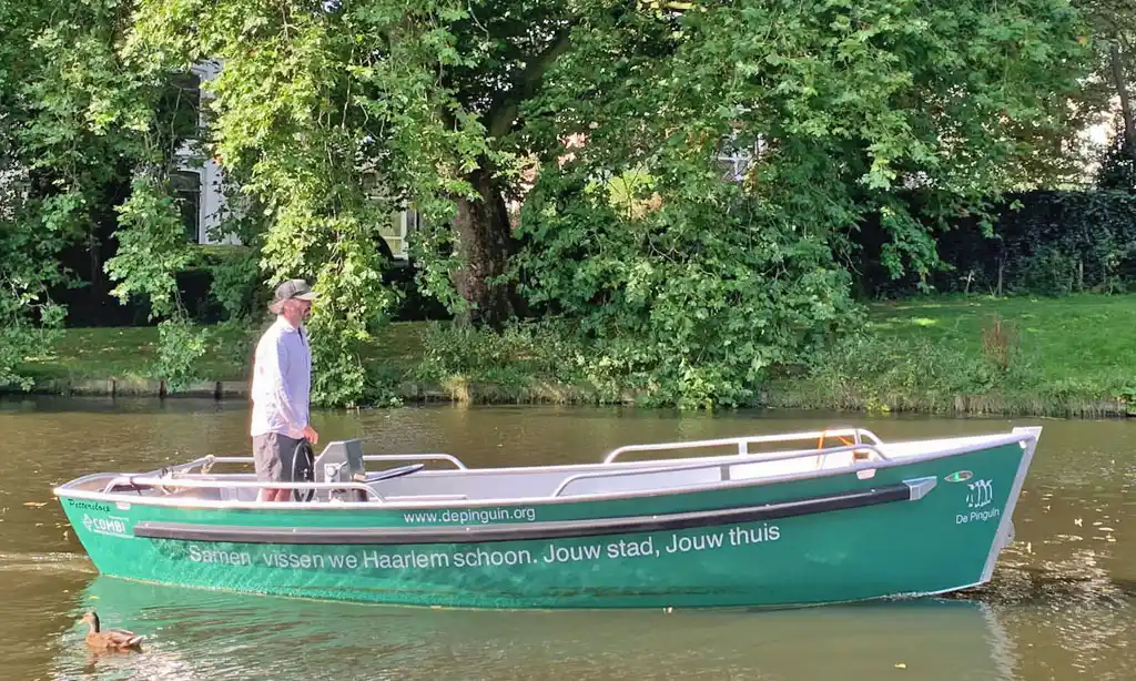 Peter sailing the De Pinguin sloop in Haarlem, a green boat on which is written “Samen vissen we Haarlem schoon. Jouw stad, Jouw thuis.”