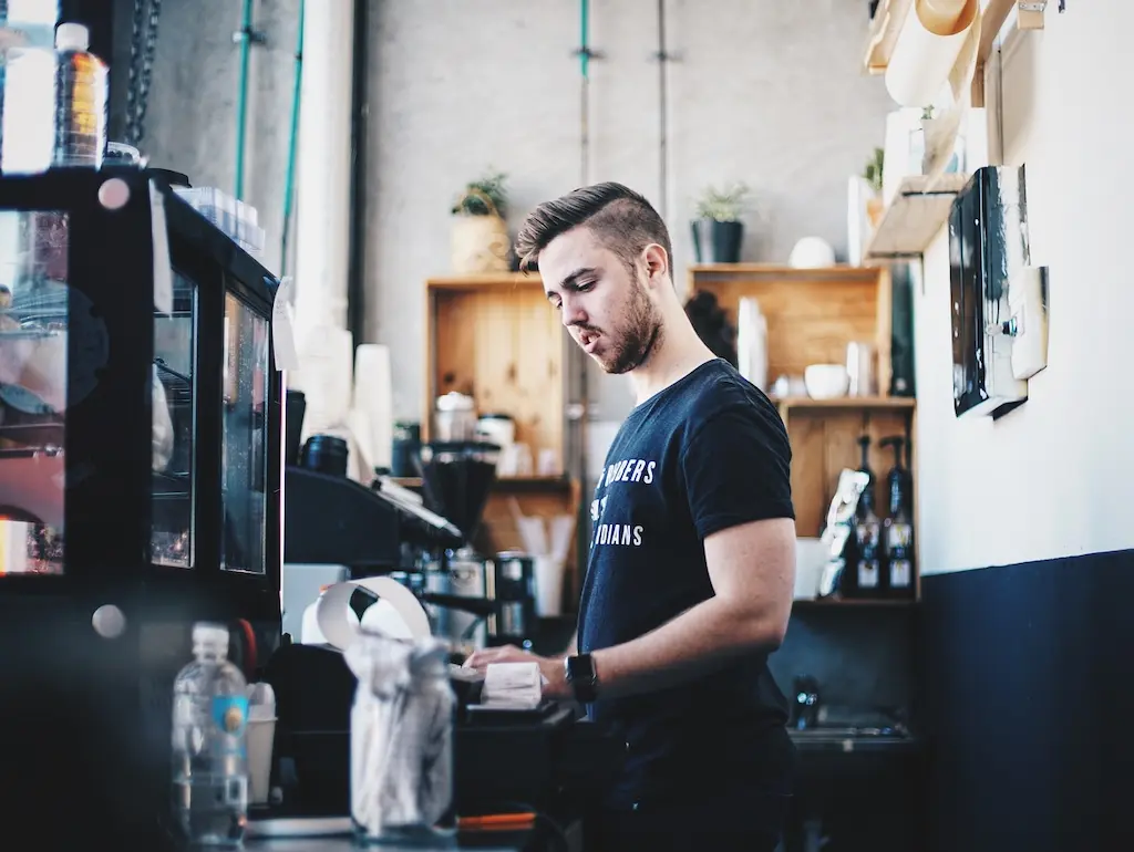 Employee working behind the counter in an independent café preparing to measure and improve its impact with a B Corp Consultant.