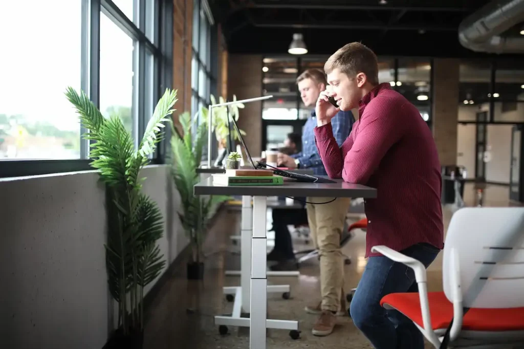 Two people working at standing desks in an office with one talking on the phone, suggesting professional services.