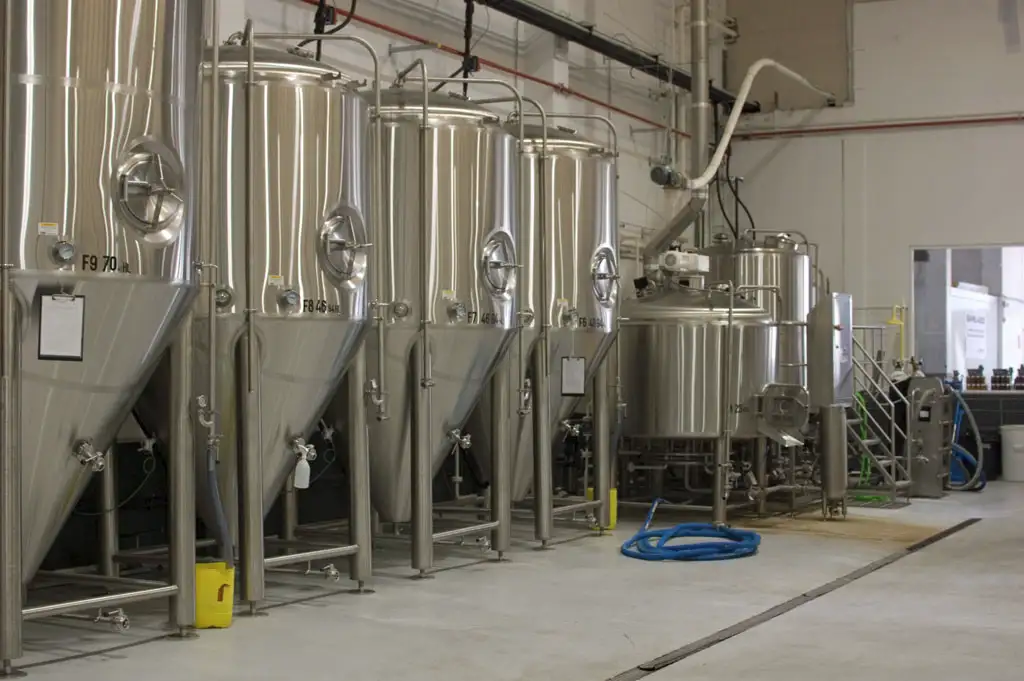 Stainless-steel fermentation tanks and brewhouse equipment inside a modern brewery considering B Corp support.