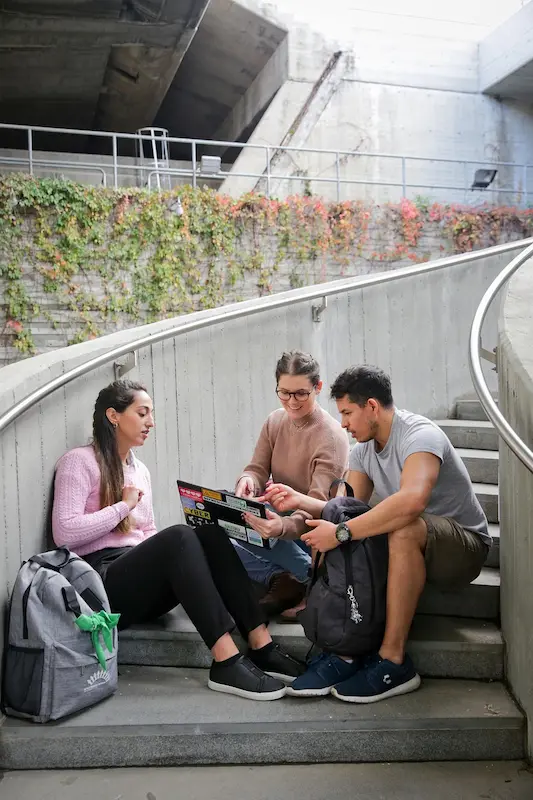 Three people collaborate on business practices over a laptop while seated on outdoor steps.