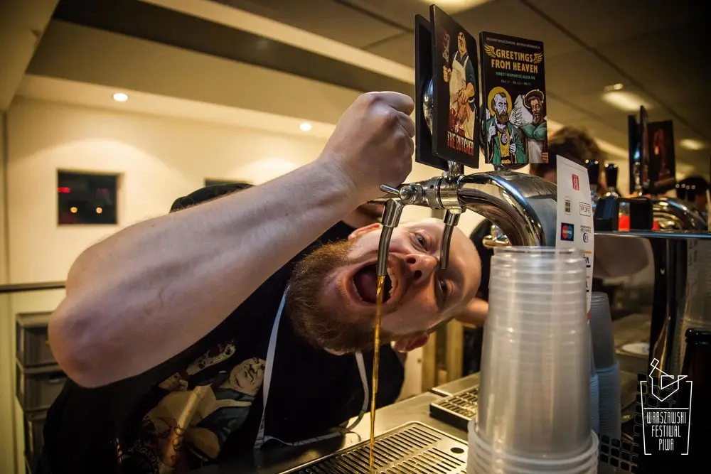 Bartender playfully posing beneath a beer tap while pouring a drink at a festival bar, capturing Fresh brewing originality & talent.